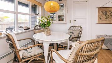 A dining area with wicker chairs, a round white table, and a hanging yellow lamp.