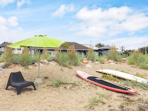 A sandy beach area with a green umbrella, a black plastic chair, and two surfboards. - 4 Star Holiday Home in Karrebaeksminde (Karrebæksminde)