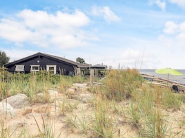 Una casa de playa con un ventanal grande, un espacio exterior cubierto y un primer plano arenoso con pastos altos.
