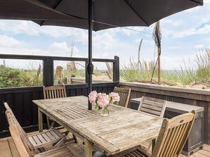 An outdoor wooden deck with a table and chairs, a black umbrella, and a view of the beach. - 4 Star Holiday Home in Karrebaeksminde (Karrebæksminde)