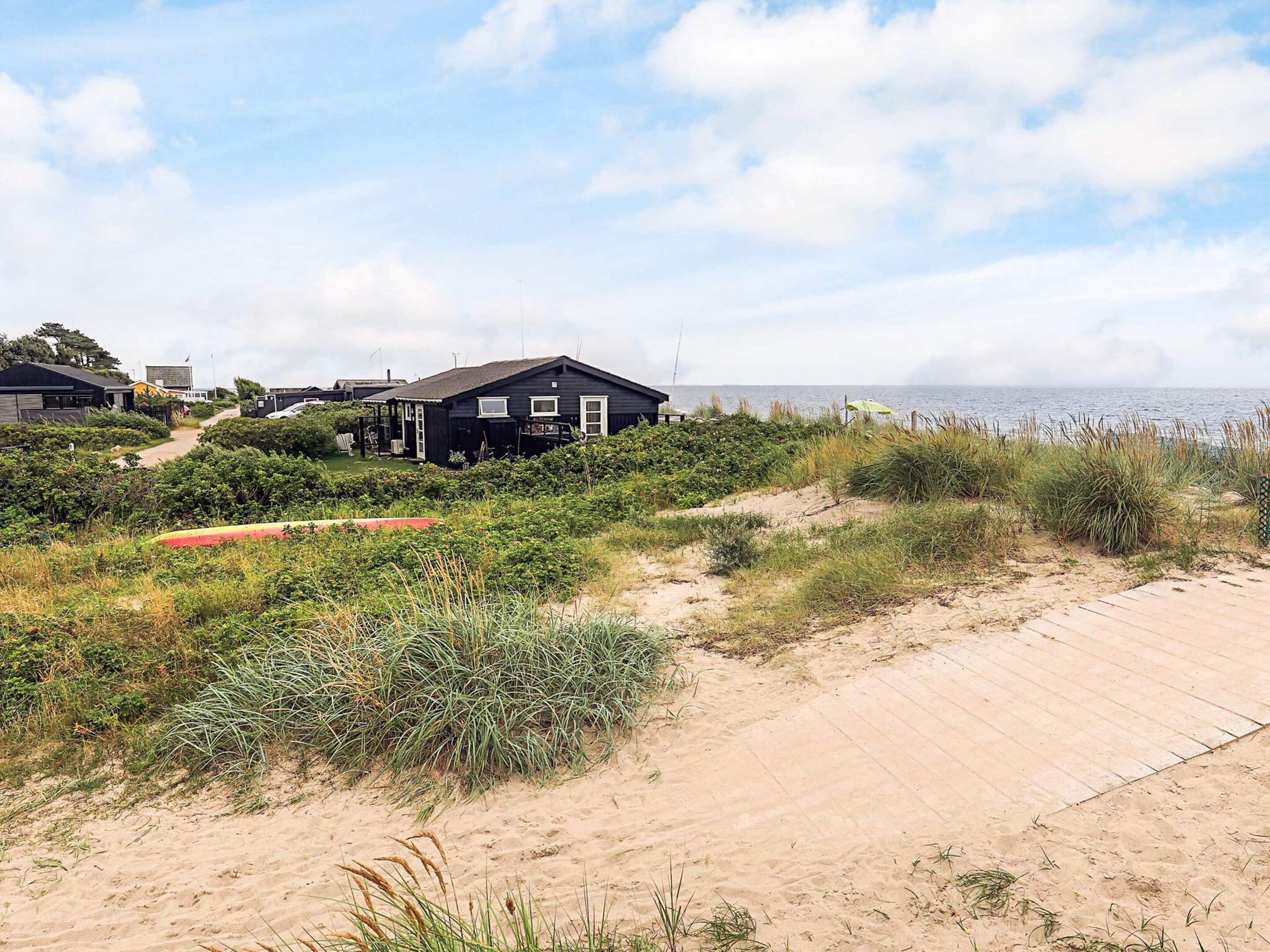 A coastal area with a sandy beach, a wooden boardwalk, and several black houses with white trim.