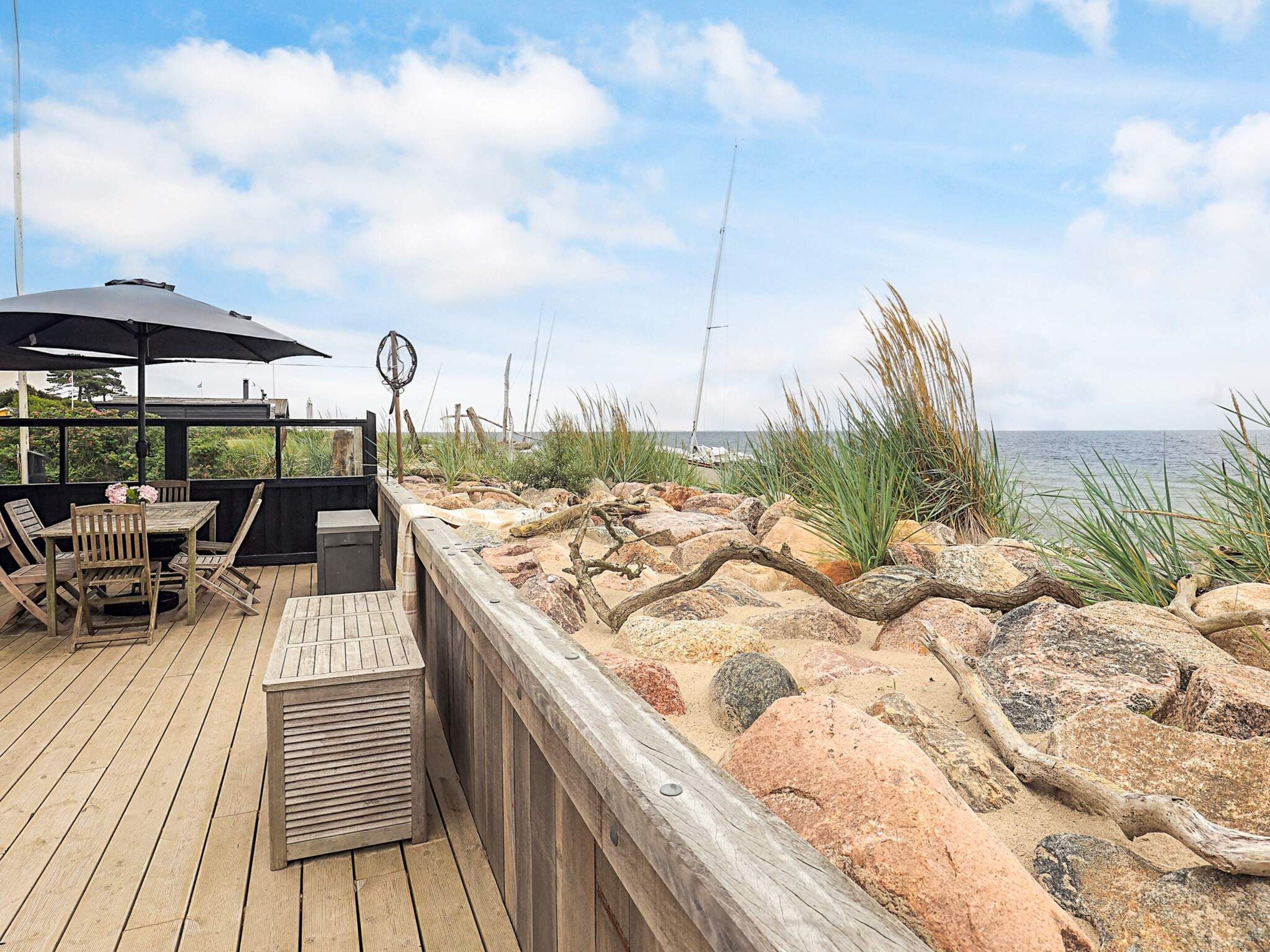 Eine Holzterrasse mit Gartenmöbeln und Blick aufs Meer.