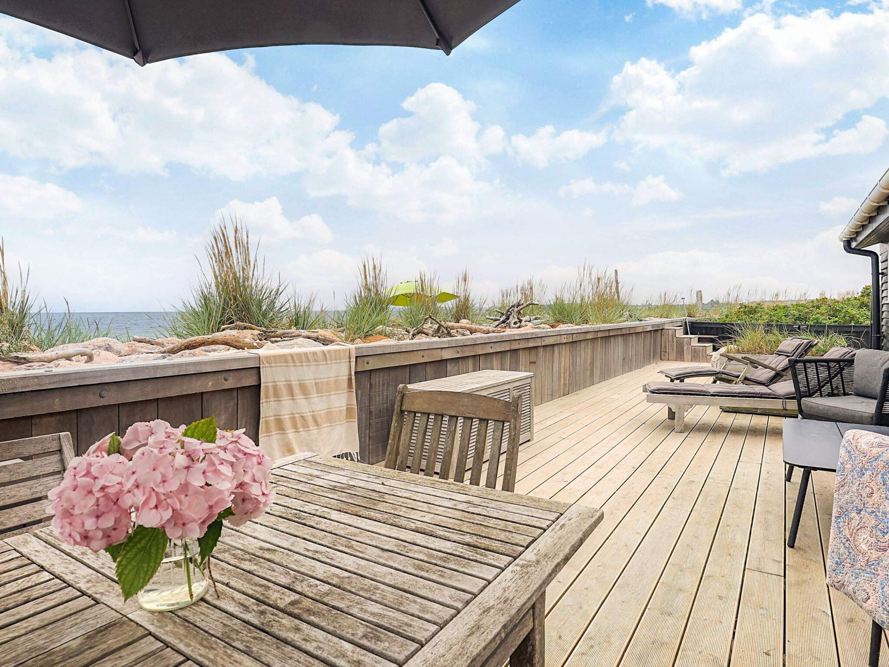 A wooden deck with a table and chairs, a grill, and a view of the ocean.