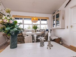 Un comedor con una mesa redonda, sillas de mimbre, una lámpara colgante y un jarrón con flores.