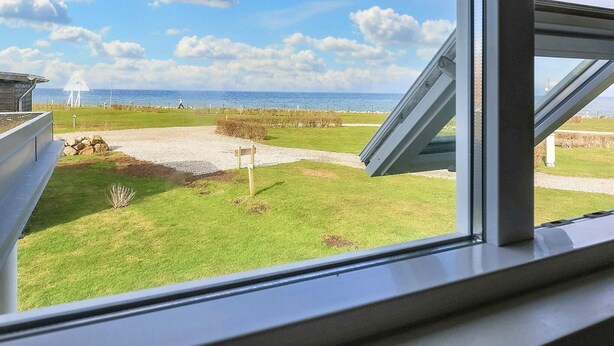 A view from a window overlooking a grassy area with a clear sky and a body of water in the distance. - 4 Person Holiday Home in Bogense (Bogense)