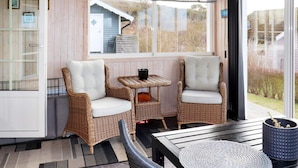 A cozy seating area with wicker chairs and a small table, a large window with a view of a house and trees, and a door leading outside. - 4 Star Holiday Home in Varberg-by Traum (Varberg)