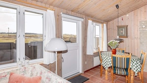 Une pièce chaleureuse avec un plafond en bois, un canapé à motifs floraux, une table à manger avec des chaises et de grandes fenêtres avec des rideaux.