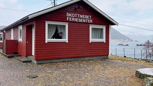 A red building labeled 'SKOTTNESET FERIESENTER' with two windows and a gravel ground. - 3 Person Holiday Home in Flatraket (Stad)