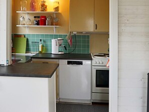 A compact kitchen with a dishwasher, a stove, and a coffee maker. There are shelves above the counter holding jars and a red box. - 6 Person Holiday Home in Mellbystrand (Mellbystrand)