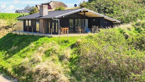 Ein modernes Haus mit einer großen Glasfassade, einer überdachten Terrasse und Blick auf die umliegende Landschaft.