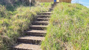 Eine Treppe aus Stein führt zu einer modernen Holzbeschreibung mit geneigtem Dach, umgeben von einer grasbewachsenen Fläche.