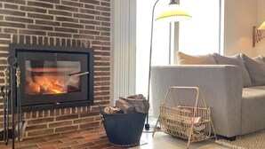 Ein Wohnzimmer mit Kamin aus Ziegelsteinen, einem grauen Sofa, einer Stehlampe und einem Korbkorb mit Holzscheiten.
