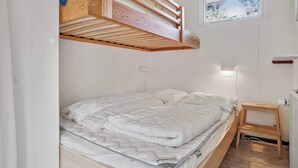 Een stapelbed met houten frame en wit beddengoed, een klein nachtkastje en een raam met uitzicht op bomen.