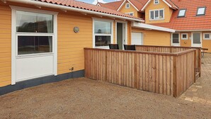 Fileira de casas amarelas com telhados de telha vermelha, cercas de madeira e chão de cascalho.
