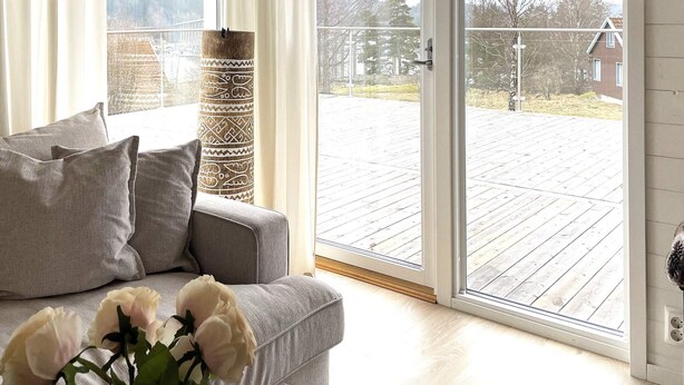 A living room with a grey sofa, a vase with white flowers, and a view through a sliding glass door to an outdoor deck. - 4 Star Holiday Home in Uddevalla (Uddevalla)