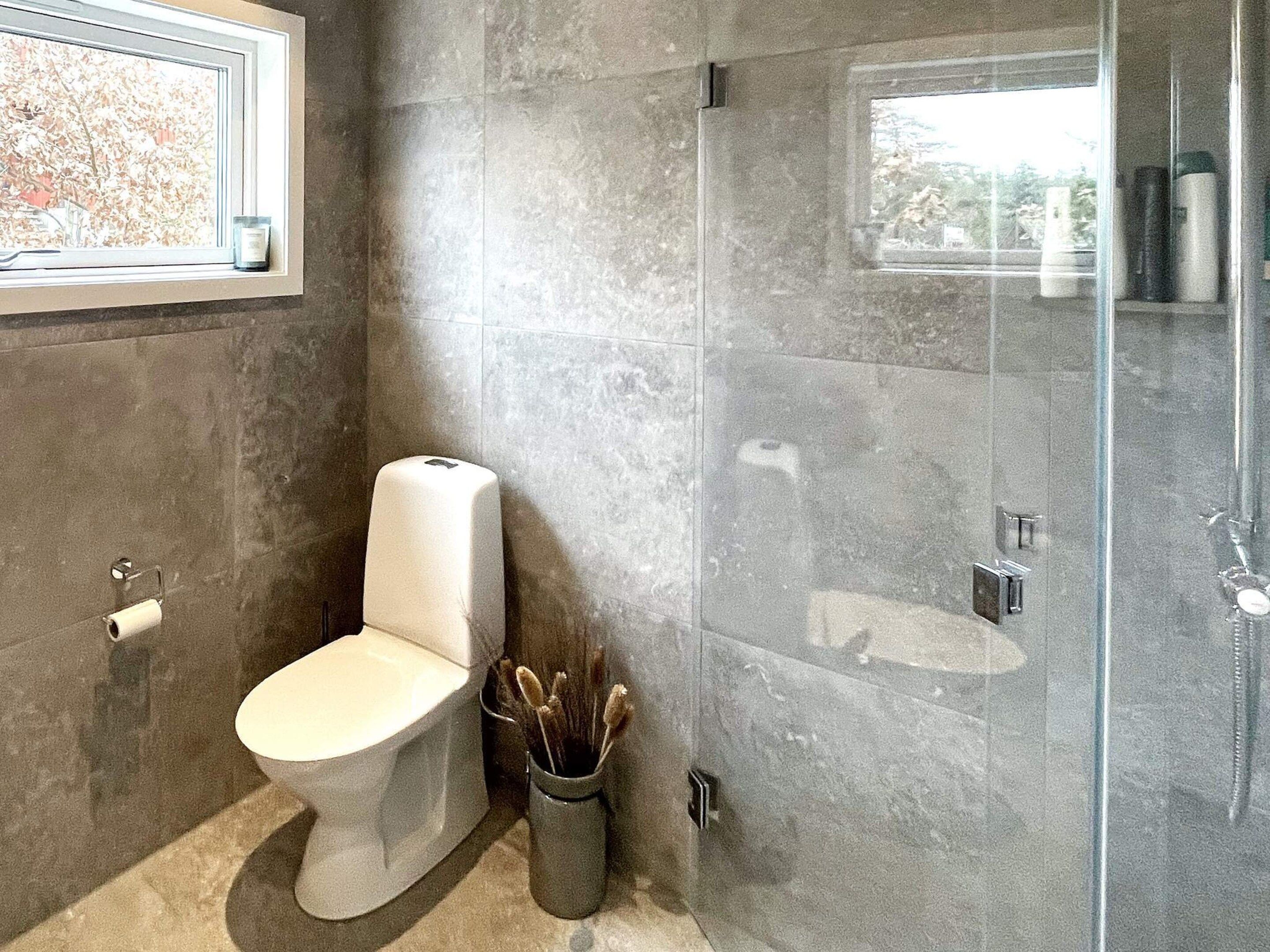 Une salle de bain avec des toilettes, une douche à parois de verre et une fenêtre.