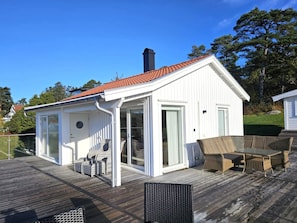 A white building with a red-tiled roof, a covered patio with wicker furniture, and a wooden deck.