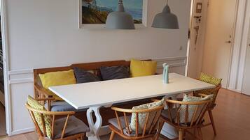 A dining area with a white table, four wicker chairs, a bench with cushions, and two pendant lights.