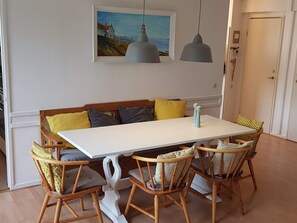 A dining area with a white table, four wicker chairs, a bench with cushions, and two pendant lights.