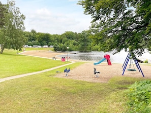 A park with a playground, a sandy area, a path, and a lake in the background. - 4 Star Holiday Home in Olofstrom (Olofström)