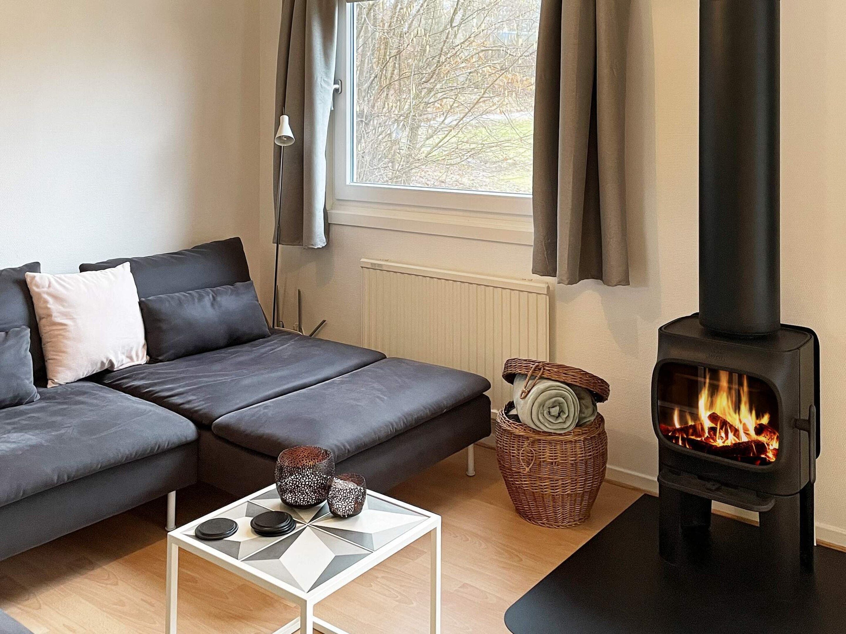 Una sala moderna con sofá, una mesita, chimenea y ventana con cortinas.