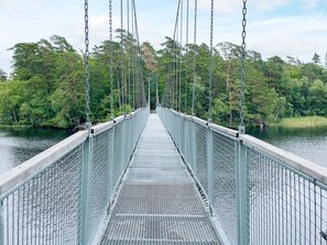 A suspension bridge with metal railings and a walkway over a body of water, surrounded by dense greenery.