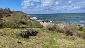 Un paysage côtier caractérisé par une côte rocheuse, des zones herbeuses et un ciel dégagé.