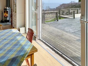 A room with a wooden table and chairs, a fireplace, and a view of a wooden deck and beach. - 4 Star Holiday Home in Arild-by Traum (Arild)