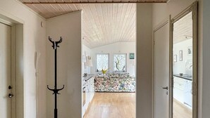 Un couloir mène à une cuisine dotée d’un plancher en bois, d’un porte-manteau et offrant une vue sur l’espace cuisine.