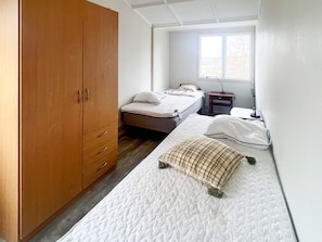 Une chambre avec deux lits, une armoire, un bureau et une fenêtre.