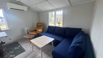 A living room with a blue sofa, a brown leather chair, a small wooden table, and a window with a view of greenery.