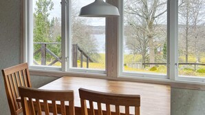 A dining area with a wooden table and chairs, large windows with a view of trees and a lake, and a pendant light. - 4 Person Holiday Home in Lekeryd (Lekeryd)