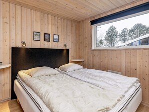 A bedroom with a wooden paneled wall, a large bed with white bedding, and a window with a view of trees. - 4 Star Holiday Home in Albaek (Aalbaek)