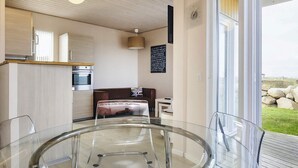 A modern kitchen with wooden cabinets, a built-in oven, and a dining area with a glass table and chairs. - 4 Person Holiday Home in Bogense (Bogense)