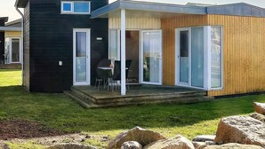 A modern two-story house with a black exterior and wooden accents, featuring a patio with outdoor seating and a large sliding glass door. - 4 Person Holiday Home in Bogense (Bogense)