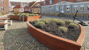 A cobblestone courtyard with a wooden planter, a bench, and a metal sculpture. - 4 Person Holiday Home in Bogense (Bogense)