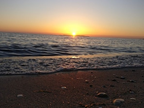 A beach at sunset with the sun near the horizon, calm water, and a sandy shore with scattered debris. - 4 Star Holiday Home in Logstor (Logstor)