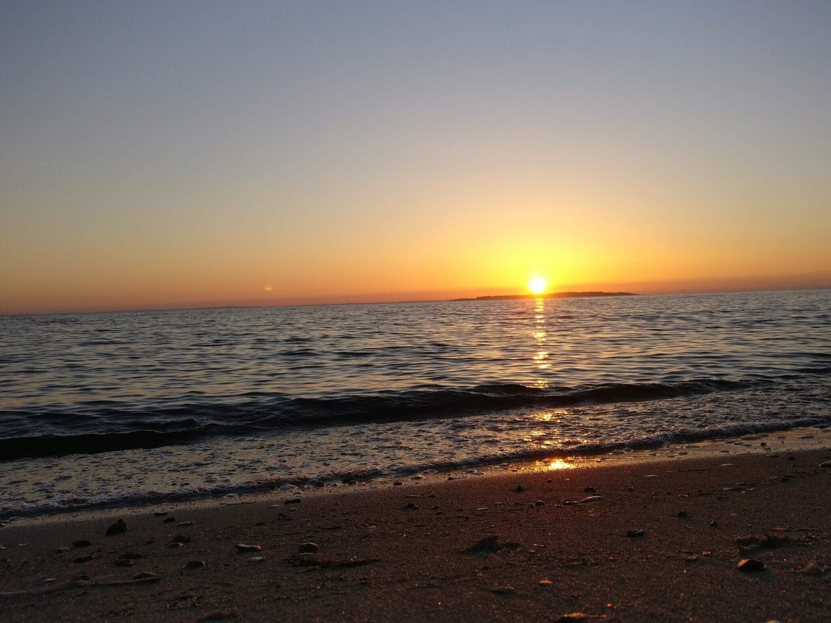 A beach with the sun setting over the ocean, creating a calm and serene atmosphere.