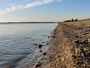 A pebbly beach with calm water, distant wind turbines, and a clear sky. - 4 Star Holiday Home in Logstor (Logstor)