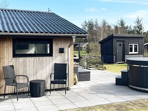 A wooden building with a metal roof, outdoor seating with chairs and a table, and a small structure with a window. - 4 Star Holiday Home in Logstor (Logstor)