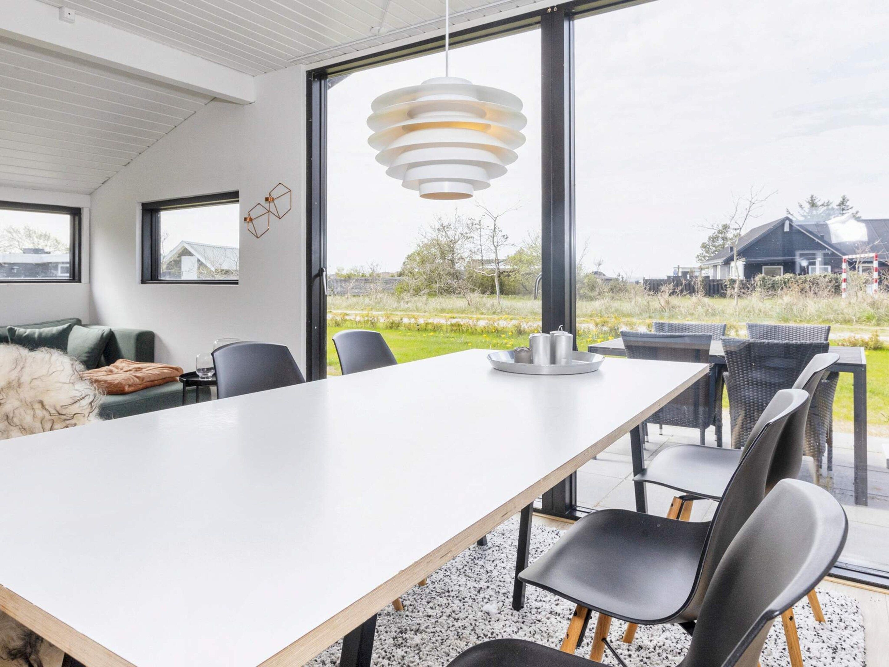 Een moderne eetruimte met een lange tafel, zwarte stoelen en een hanglamp.