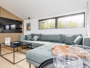 A modern living room with a sectional sofa, a coffee table, and a large window providing a view of trees. - 4 Star Holiday Home in Logstor (Logstor)