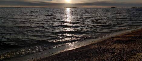 A beach with the sun reflecting on the water, a distant shoreline, and a clear sky.