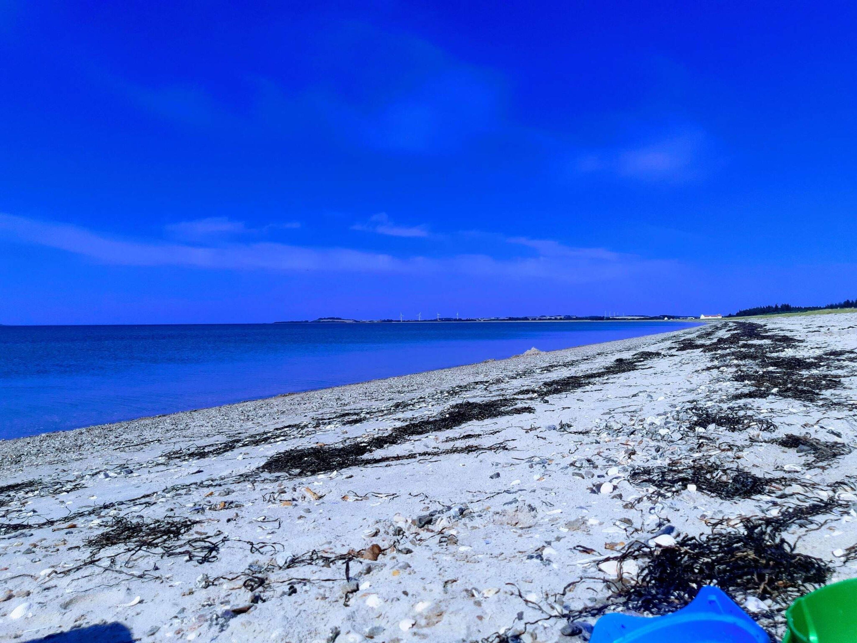 A beach with a clear sky, calm sea, and rocky shoreline.