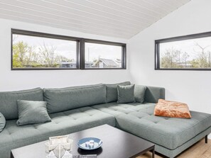 Een moderne woonkamer met een grijze modulaire bank, een salontafel en twee ramen met uitzicht op bomen en gebouwen.