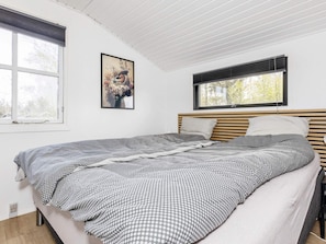 Een slaapkamer met een bed, een raam met zonwering, een aan de muur hangend schilderij en een plafond met houten latten.