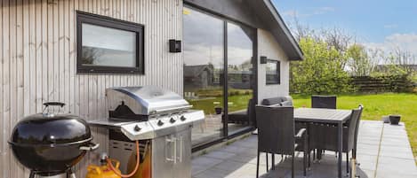 An outdoor patio with a barbecue grill, a gas tank, and a table with chairs.
