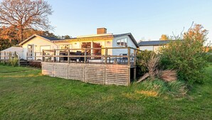 Une maison à deux étages avec une terrasse, une cheminée et une grande fenêtre.