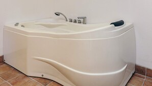 Une grande baignoire sur pieds, dotée d’un seul robinet et de boutons de commande, placée devant un mur sobre et sur un sol carrelé.