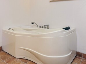 Eine große, freistehende Badewanne mit einem einzelnen Wasserhahn und Armaturen, vor einer schlichten Wand mit Fliesenboden.